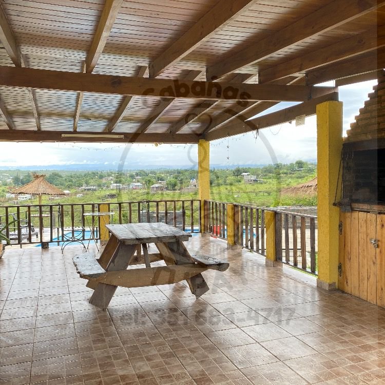 Amplia galería exterior techada con asador privado de ladrillo y mesa de madera frente al paisaje serrano.