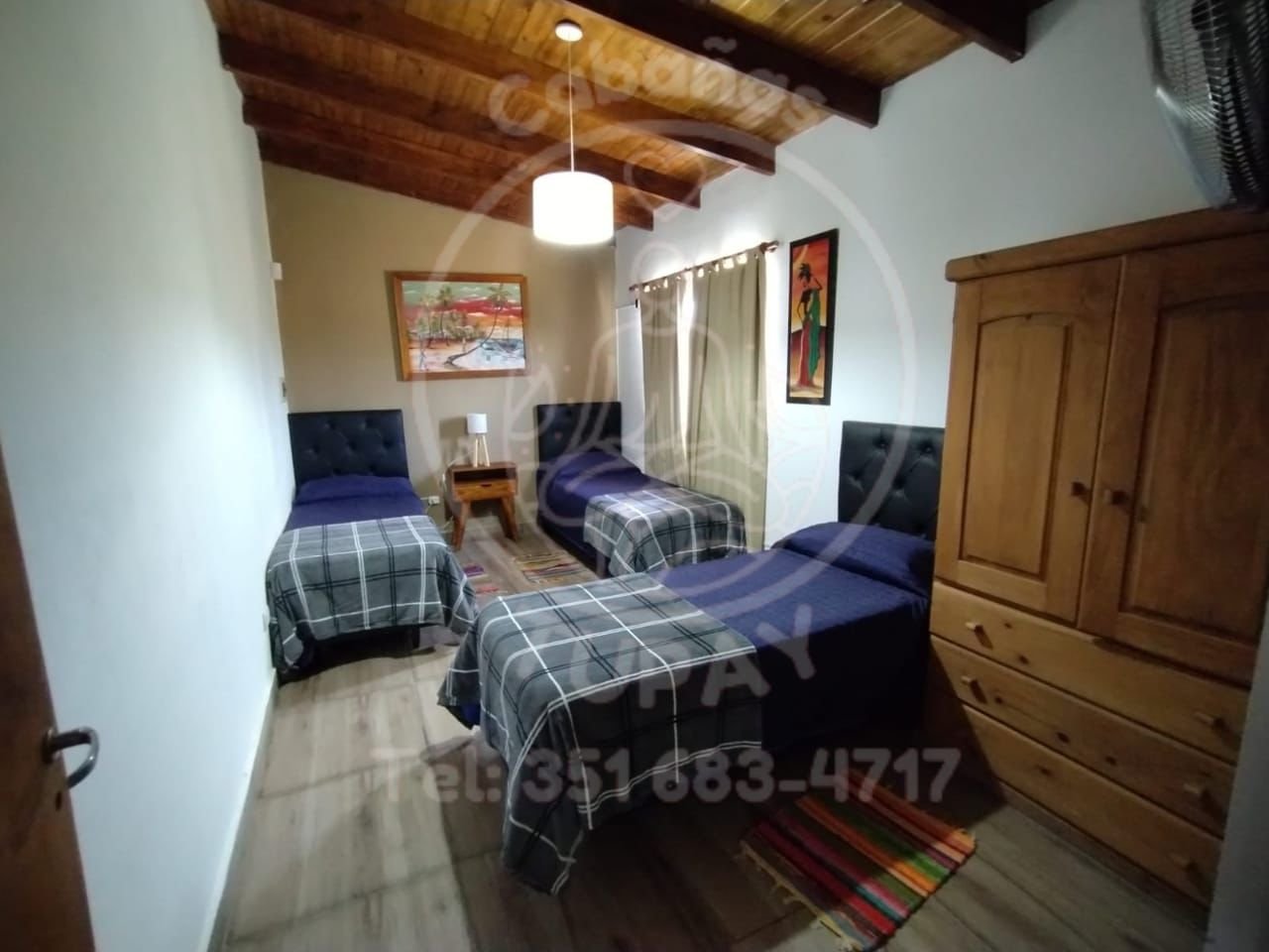 Amplio dormitorio secundario en planta alta con tres camas individuales, techos de madera y decoración cálida.