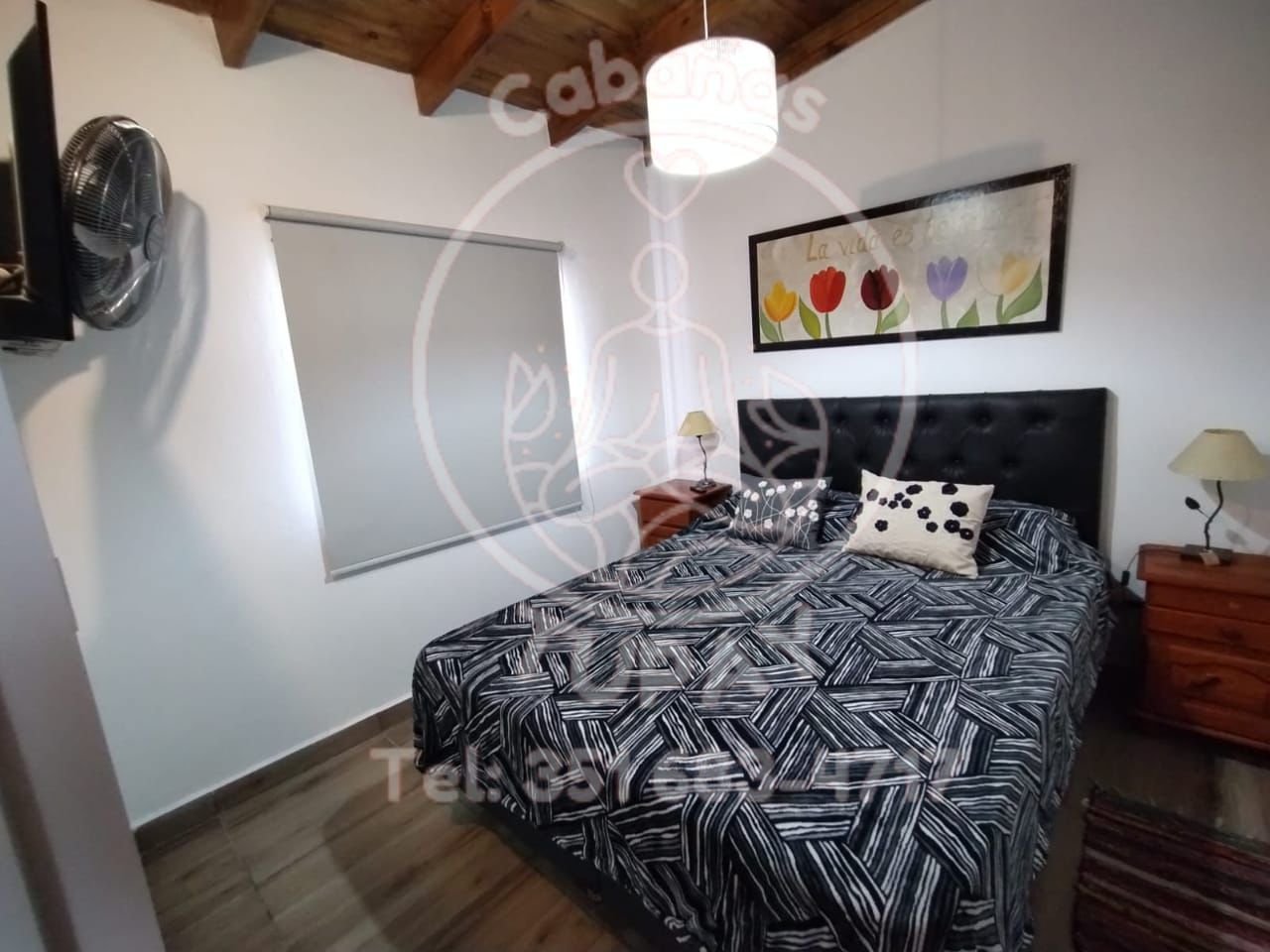 Habitación matrimonial luminosa con sommier, respaldo capitoné negro y ventana con cortinas blackout.