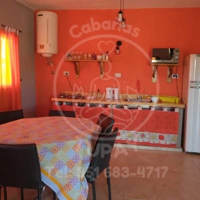 Vista completa de la cocina con pared naranja vibrante, bacha, vajilla completa y zona de preparación.