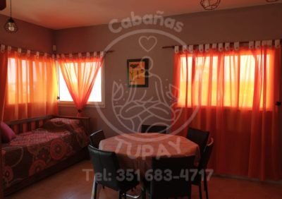 Sector de descanso adicional en el estar-comedor con cama individual y cortinas naranjas que filtran luz cálida.