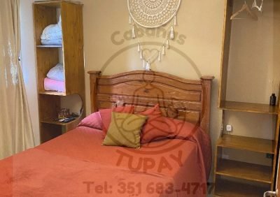 Dormitorio principal con cama matrimonial de madera, ropero abierto y decoración cálida con atrapasueños en Cabaña Naranja.