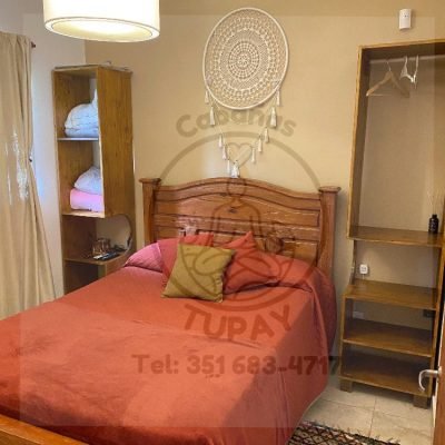 Dormitorio principal con cama matrimonial de madera, ropero abierto y decoración cálida con atrapasueños en Cabaña Naranja.