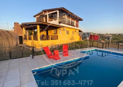 Vista exterior del complejo Cabañas Tupay mostrando la piscina cercada, solárium y la cabaña de dos plantas al atardecer.