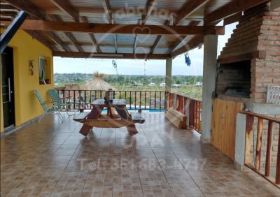 Galería techada privada con asador parrilla y mesa de madera con vistas panorámicas a las sierras en Cabaña Green, Villa Parque Siquiman.